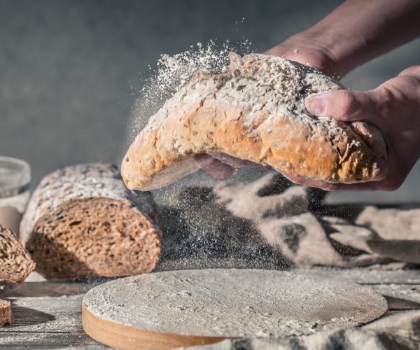 baker with flour in his hand and fresh bread on a beautiful wooden background, the concept of healthy food and bakery industry
