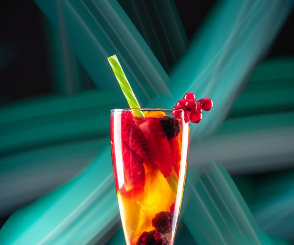 Glass with cocktail and different fresh berries on board on abstract background