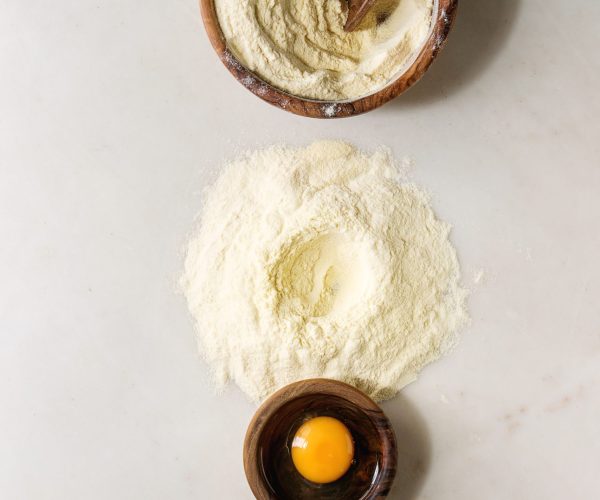 Ingredients for homemade italian pasta ravioli cooking semolina flour, egg yolk, sea salt with olive wood utensils bowls and scoopover white marble background. Flat lay, space. Home baking concept